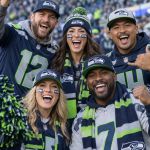 A group of Seattle Seahawks fans in authentic navy and action green gear cheering together in the stands