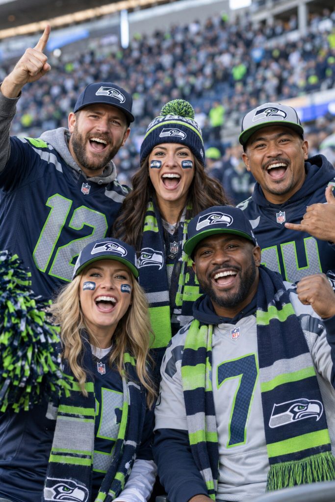 A group of Seattle Seahawks fans in authentic navy and action green gear cheering together in the stands